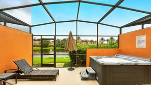 Un patio con paredes de vidrio, que incluye un jacuzzi, sillas de descanso y vistas a un lago y edificios.