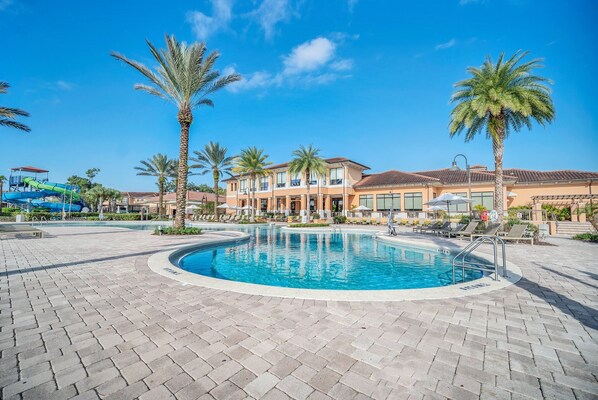A swimming pool with a tiled deck, surrounded by palm trees and a building with multiple balconies. - Vacation Heaven Close 2 Disney~waterslides & pool (Kissimmee)