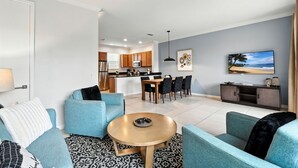 Una sala de estar moderna con sofás azules, una mesa de centro redonda y una cocina al fondo.