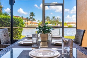 Mesa lista para comer con vista a un cuerpo de agua y palmeras.