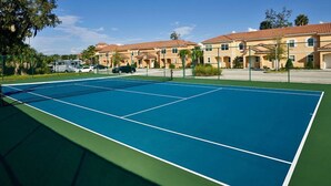Een tennisbaan met een groen en blauw oppervlak, omringd door gebouwen met rode dakpannen.