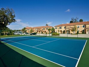 Een tennisbaan met een groen en blauw oppervlak, omringd door gebouwen met rode dakpannen.
