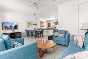 A modern living room with a dining area, kitchen, and a flat-screen TV displaying a cityscape.
