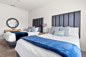 Quarto de hotel com duas camas, um espelho redondo, mesa de cabeceira com abajur e cabeceira com painéis verticais.