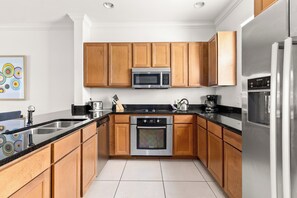 A modern kitchen with wooden cabinets, stainless steel appliances, and a black countertop.