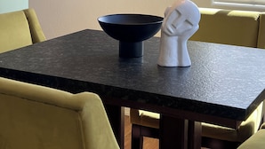 Et spiseområde med et bord, stole, en skål, en skulptur og billedkunst på væggen.