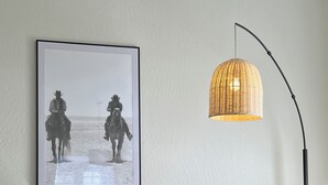 En stue med et billede i ramme af to personer på hesteryg, en moderne lampe og et træsofabord.