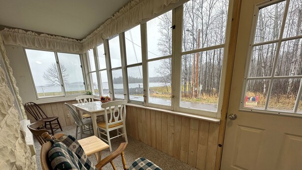 A cozy room with a wooden interior, a dining table with chairs, a cushioned bench, and large windows offering a view of trees and a body of water. - Spacious 4-bedroom house in charming Montreal across from The Gile Flowage (Montreal)