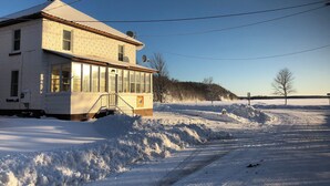 A two-story building with a snow-covered roof and a satellite dish. There is a clear sky and a snow-covered landscape in the background. - Spacious 4-bedroom house in charming Montreal across from The Gile Flowage (Montreal)
