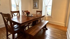 A dining room with a wooden table and chairs, a bench, and a window with curtains. - Spacious 4-bedroom house in charming Montreal across from The Gile Flowage (Montreal)