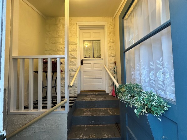 Un escalier avec une porte blanche en haut, un mur bleu orné d’un motif floral et une plante sur la droite.