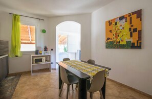 Un coin repas comprenant une table, des chaises, un four à micro-ondes et un rideau vert.