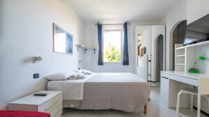 Une chambre à coucher avec un lit, un bureau et une chaise. Il y a une fenêtre avec des rideaux, une table de chevet et une chaise rouge.