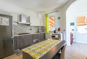 Une cuisine moderne avec des meubles gris, un réfrigérateur en acier inoxydable, une cuisinière à gaz et une table à manger recouverte d’une nappe à motifs.