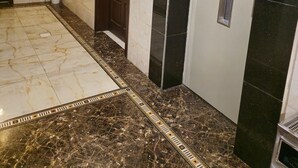 Um corredor com piso de mármore, um vaso de planta, uma porta e um elevador.