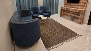 Uma sala de estar moderna com um sofá seccional, duas poltronas, uma mesa de centro e uma TV de tela plana fixada numa parede de madeira.