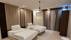 Quarto de hotel com duas camas, uma mesa pequena e um ventilador de teto.