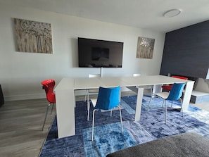 Ein stilvoller Essbereich mit einem weißen Tisch, blauen Stühlen, einem Flachbildfernseher an der Wand und Kunstwerken über dem Tisch.