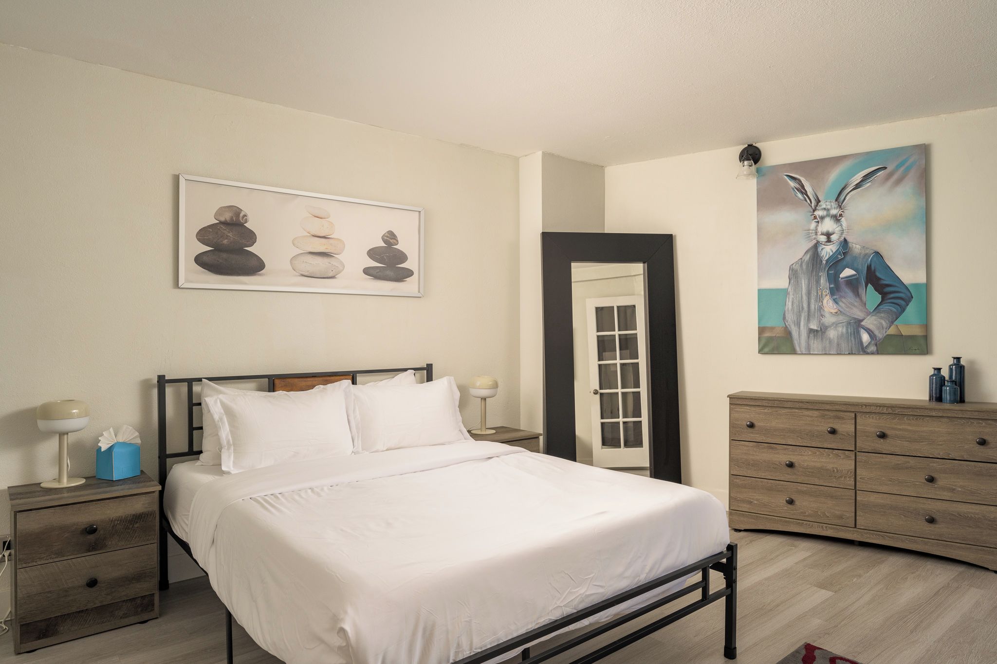 Une chambre à coucher comprenant un lit, des tables de chevet, une commode, une porte et des œuvres d’art murales.
