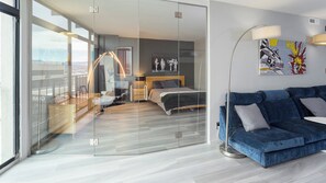 Ein modernes Schlafzimmer mit Glastrennwand, einem Bett, einem blauen Sofa und einer Lampe.