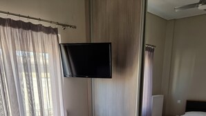 Habitación de hotel con cama, televisor montado en la pared y ventana con cortinas traslúcidas.