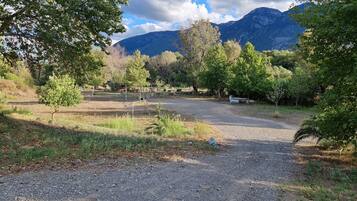A gravel path leading to a picnic area with tables and benches, surrounded by trees and mountains in the background.