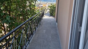 Un balcón con barandilla de metal, puerta de cristal y vista a montañas y edificios en la distancia.
