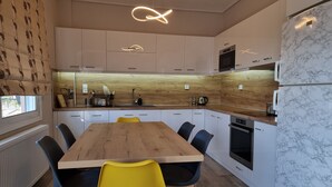 Una cocina moderna con armarios blancos, encimera de madera y salpicadero de mármol. Hay una mesa de comedor con sillas amarillas.