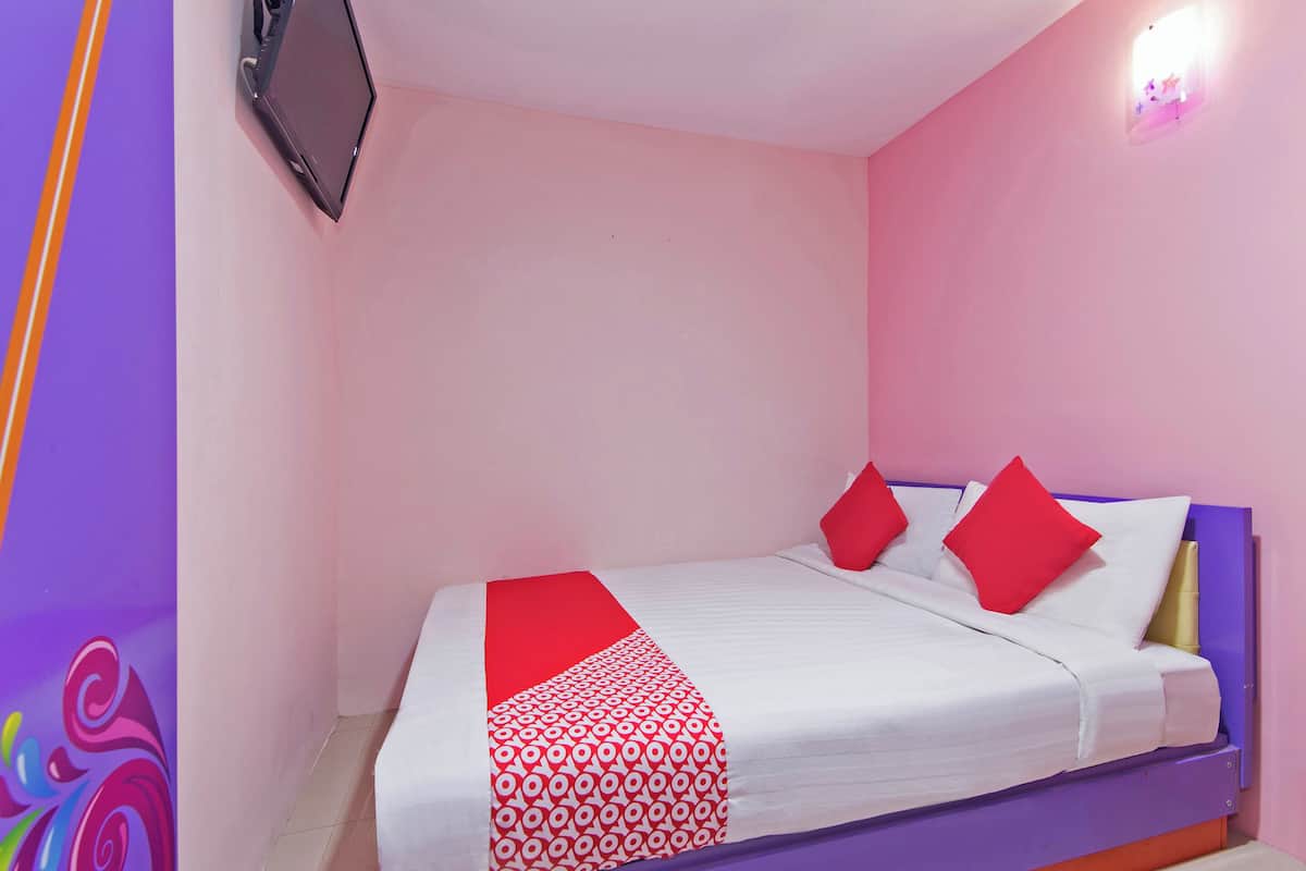 Una cama individual con ropa de cama roja y blanca, un televisor montado en la pared y una pared rosa.