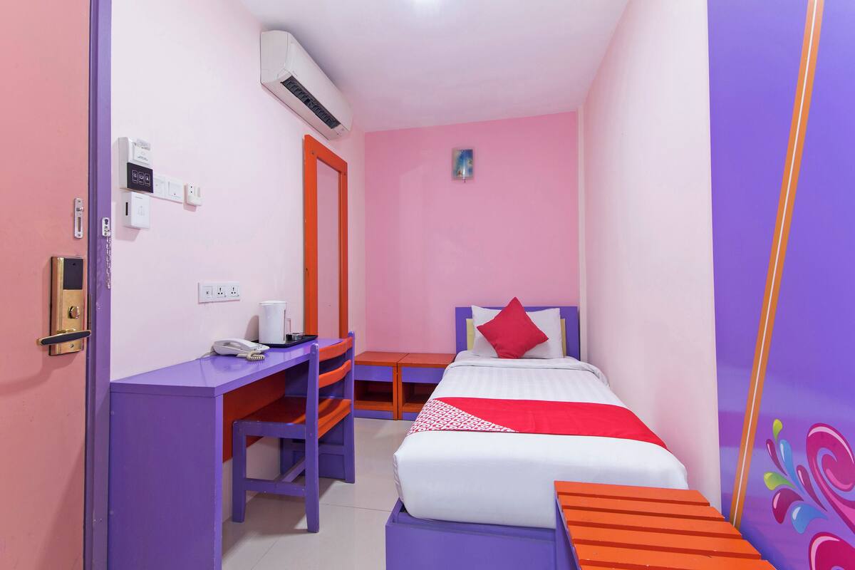 Una habitación con cama, escritorio y silla. Hay un equipo de aire acondicionado en la pared.
