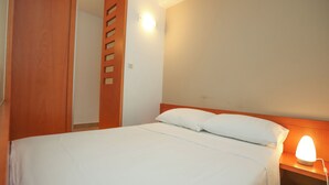 A hotel room with a bed, a nightstand with a lamp, a wooden wardrobe, and a wall-mounted light fixture. - Apartments Vallis Rabiosa  (Zadar)