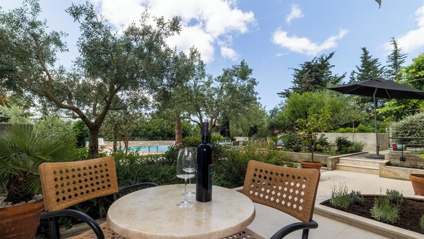 An outdoor patio with a round table and two wicker chairs, a bottle of wine, and a pool in the background. - Apartments Vallis Rabiosa  (Zadar)