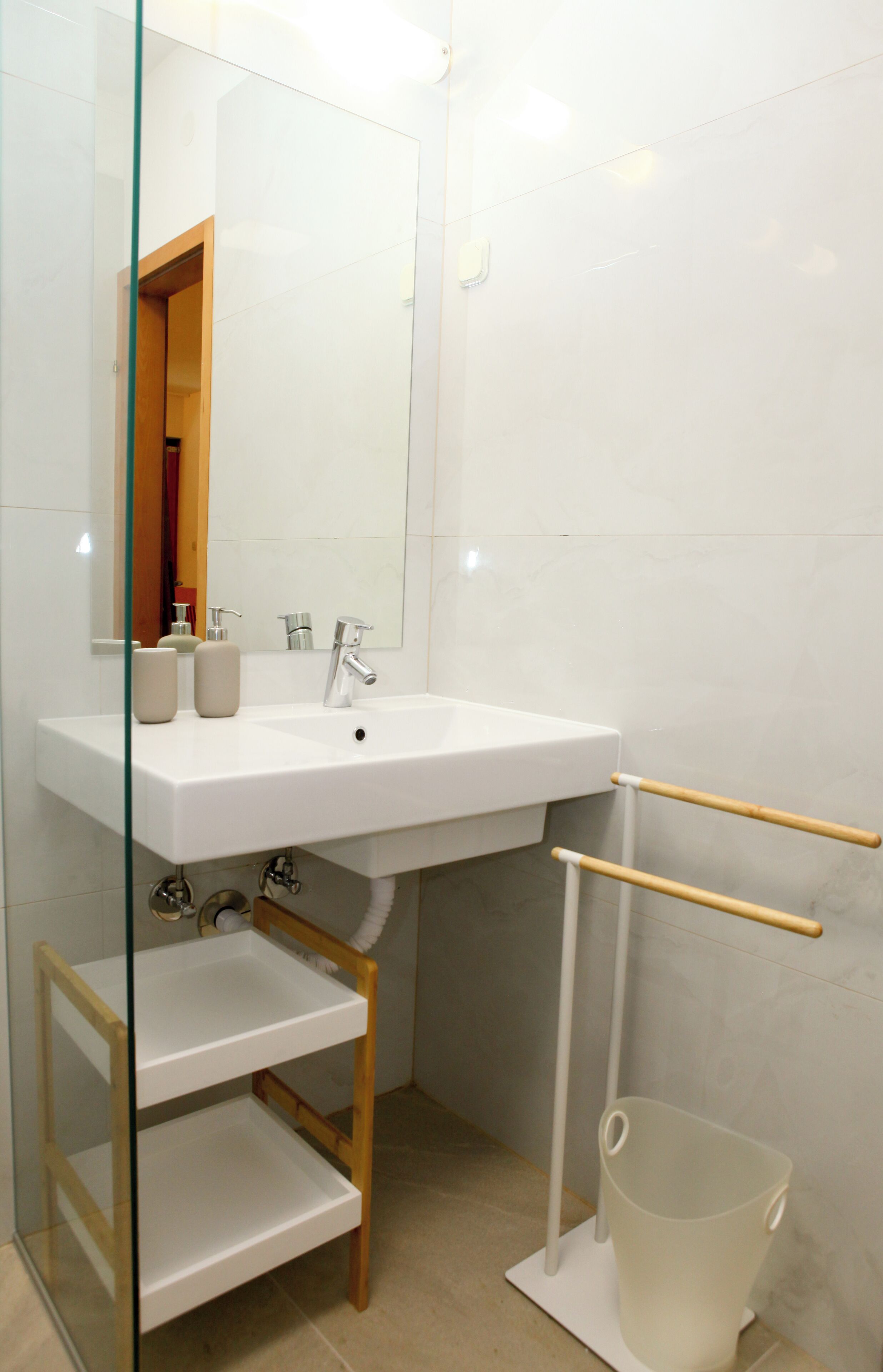 A modern bathroom with a white sink, mirror, and a wooden shelf unit.