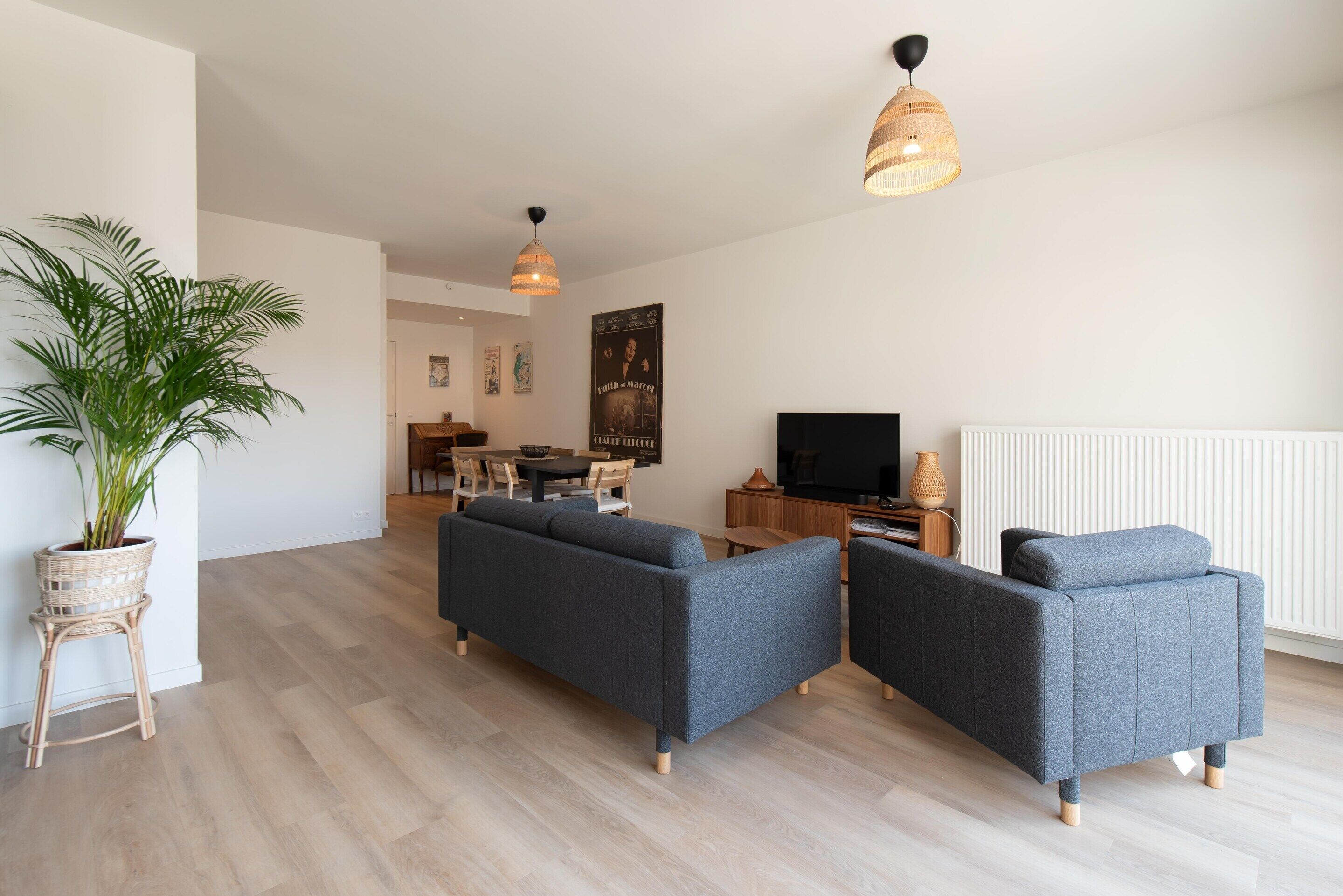 A modern living room with a sofa set, a dining table with chairs, a television, and a potted plant.
