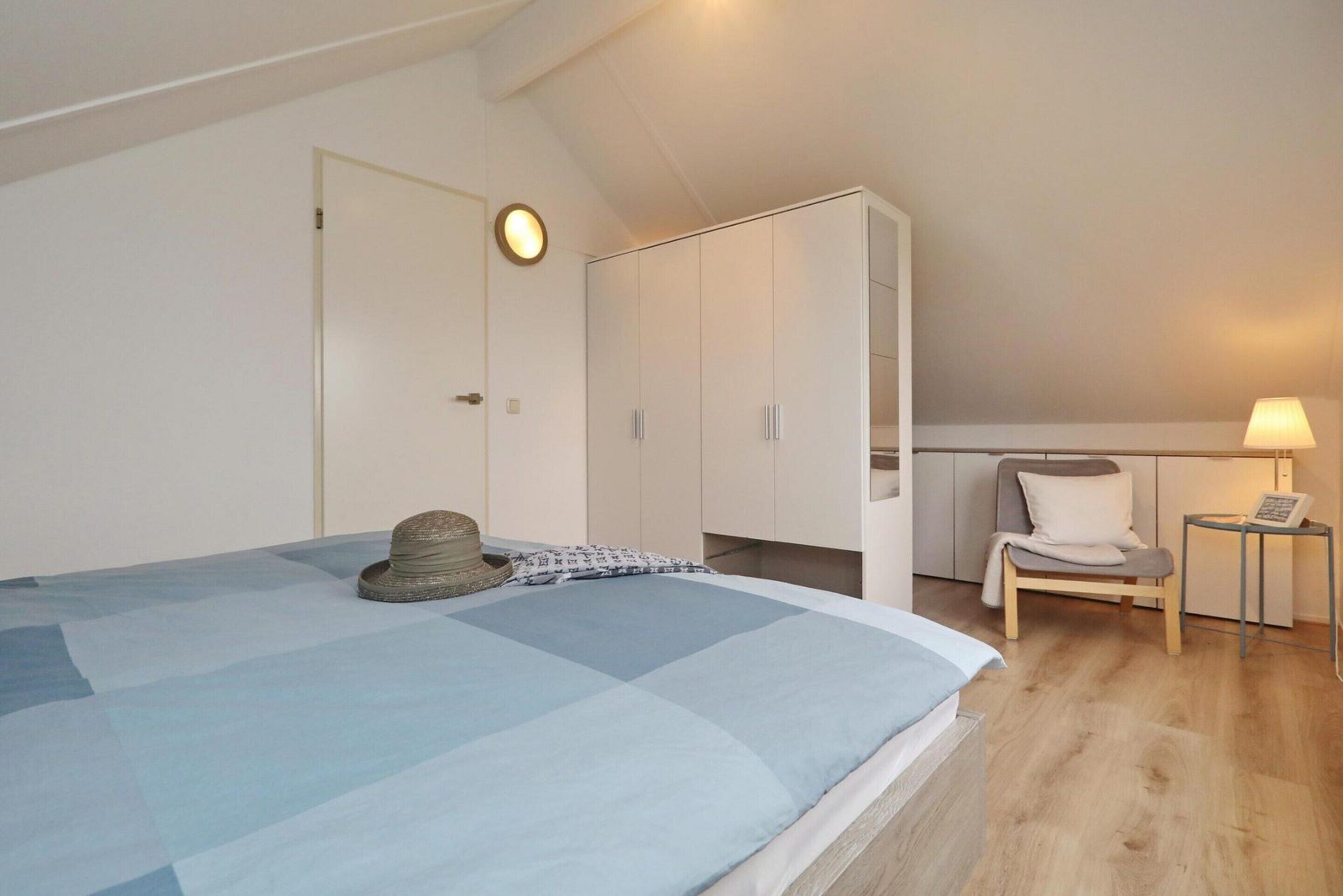 Un dormitorio con cama, armario, silla y una mesita de noche con lámpara.