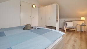 Une chambre à coucher comprenant un lit, une armoire, une chaise et une petite table avec une lampe.