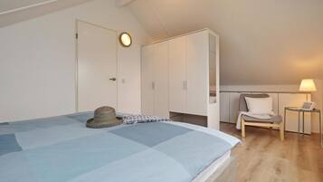 Un dormitorio con cama, armario, silla y una mesita de noche con lámpara.