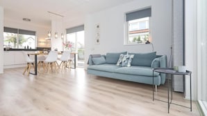 Un salon moderne avec un canapé bleu clair, un coin repas avec des chaises blanches et une cuisine en arrière-plan.