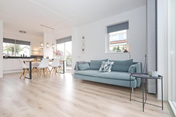 Una sala de estar moderna con un sofá azul claro, un comedor con sillas blancas y una cocina al fondo.