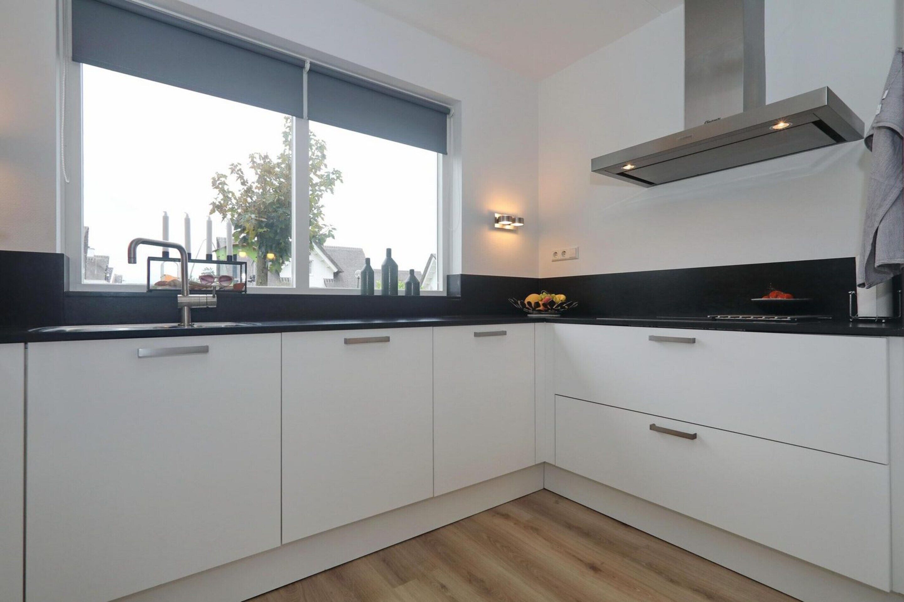 Uma cozinha moderna com armários brancos, bancada preta, janela com vista para edifícios e coifa de aço inoxidável.
