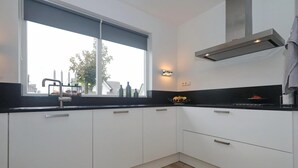 Une cuisine moderne avec des armoires blanches, un comptoir noir, une fenêtre donnant sur des immeubles et une hotte de cuisinière en acier inoxydable.