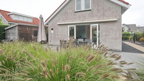 Une maison à deux étages, avec une façade en briques, un toit recouvert de tuiles rouges et une grande porte d’entrée.