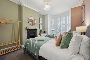 A bedroom with a bed, a wooden rack, a fireplace, a mirror, and a window with blinds. - Cosy 4-BR Home, Parking, Xbox &BBQ, for big groups (Portsmouth)