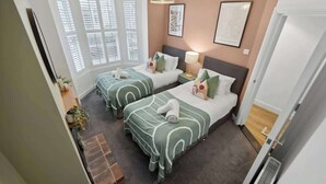 A bedroom with two beds, a window, a lamp, and a framed picture on the wall.