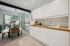 A modern kitchen with white cabinets, a wooden countertop, and a dining area with a table and chairs. - Cosy 4-BR Home, Parking, Xbox &BBQ, for big groups (Portsmouth)