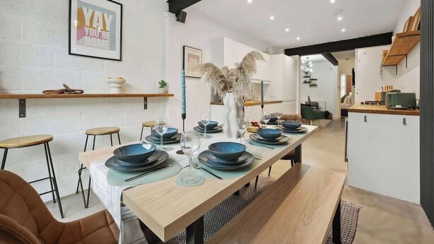 A modern kitchen with a long dining table set for six, featuring blue dinnerware and a decorative vase.
