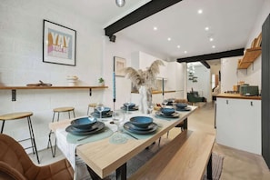 A modern kitchen with a long dining table set for six, featuring blue dinnerware and a decorative vase. - Cosy 4-BR Home, Parking, Xbox &BBQ, for big groups (Portsmouth)