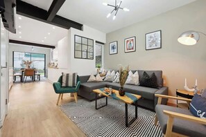 A modern living room with a sofa, coffee table, and chairs, a dining area with a table and chairs, and a large window with a view. - Cosy 4-BR Home, Parking, Xbox &BBQ, for big groups (Portsmouth)