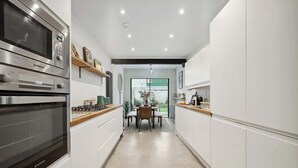 A modern kitchen with built-in appliances, a dining area with a table and chairs, and a view through a glass door.