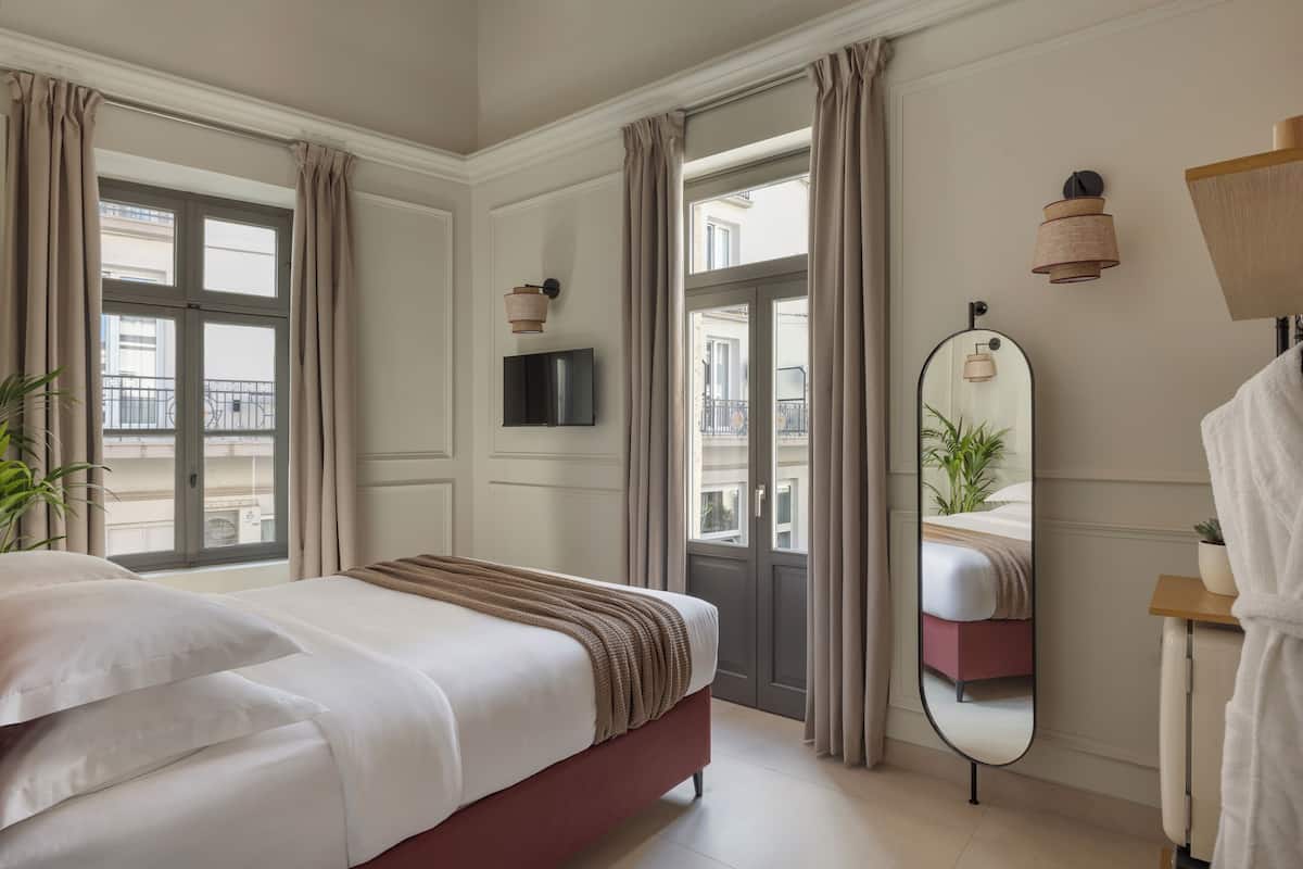 A hotel room with a bed, a mirror, a TV, and a view of the outside balcony.